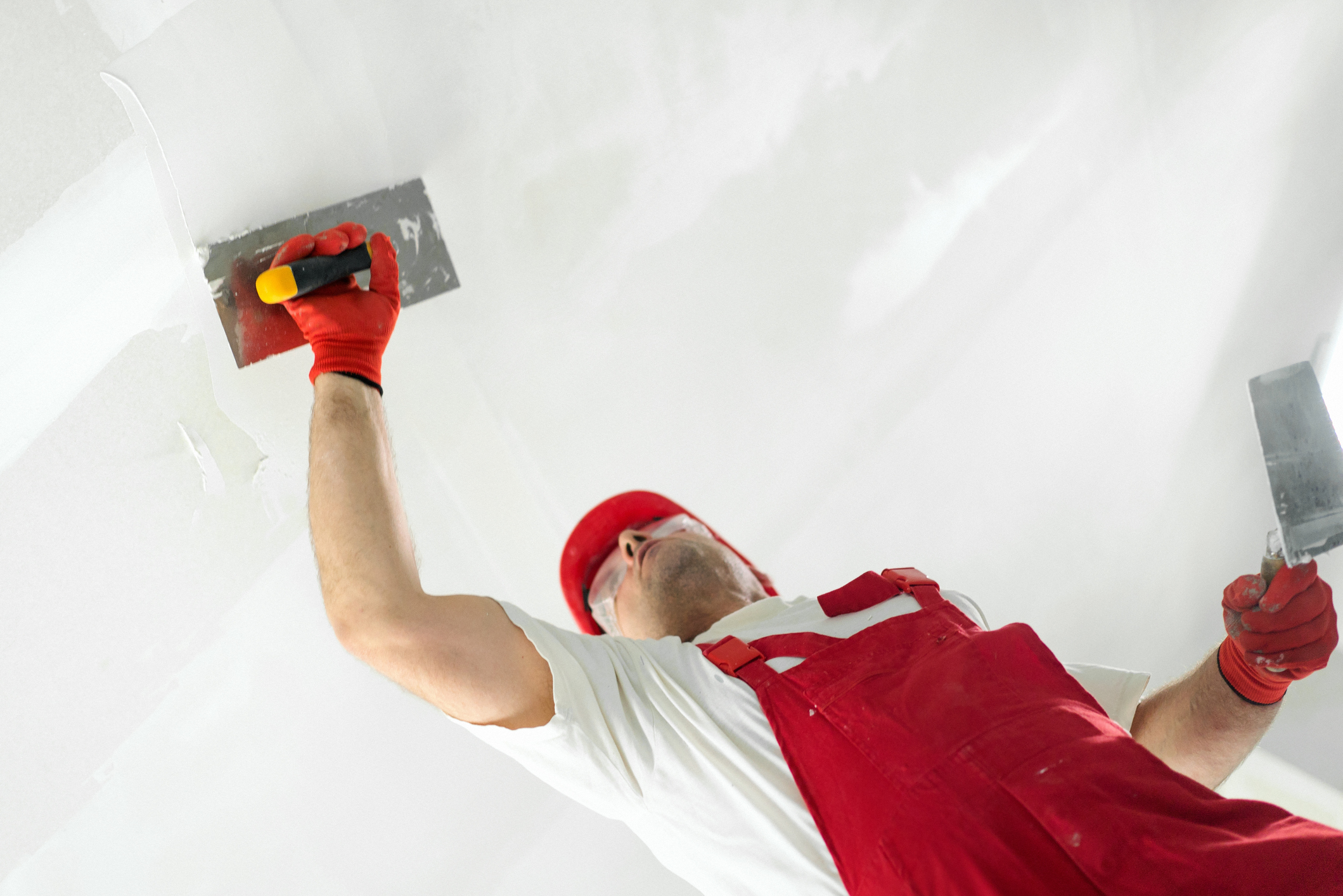 Closeup side view of a middle aged construction worker applying plaster onto a ceiling.